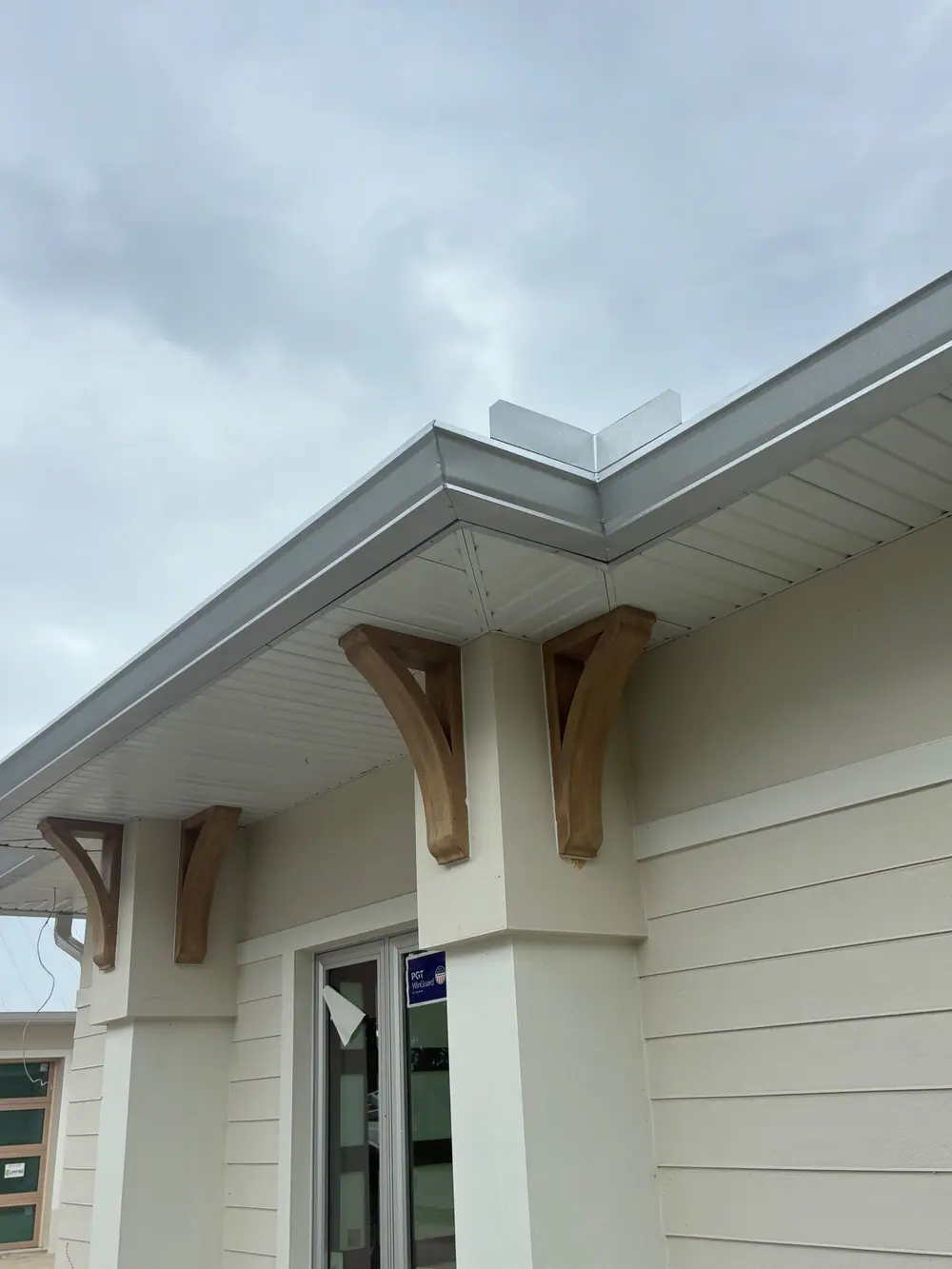 Silver gutter with a mitered outside corner above white soffit and wood brackets on a new home